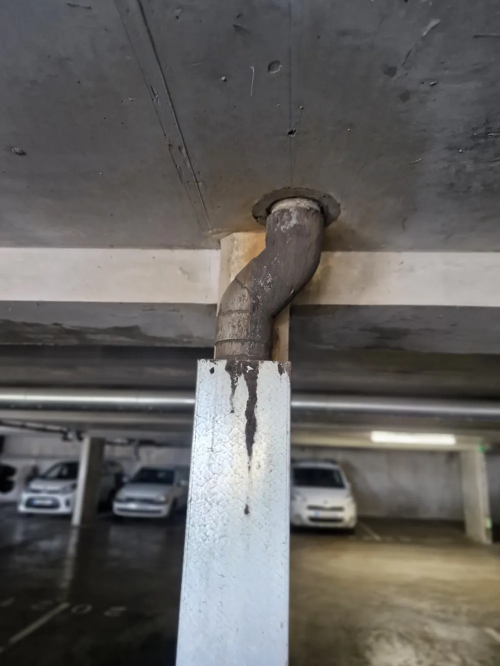 Descente d'eau pluviale dans un parking couvert, coulures sur le capot de protection