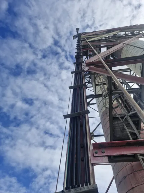Câbles et antennes fixés le long d'un pylône industriel, vus depuis le sol