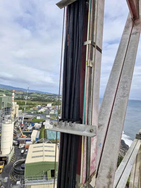 Faisceau de câbles fixé sur un pylône industriel, la côte et la mer en arrière-plan