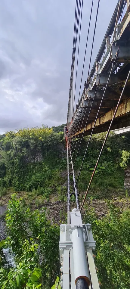 Sous le tablier du pont suspendu de Sainte-Rose, un cordiste progresse le long des câbles au-dessus de la ravine