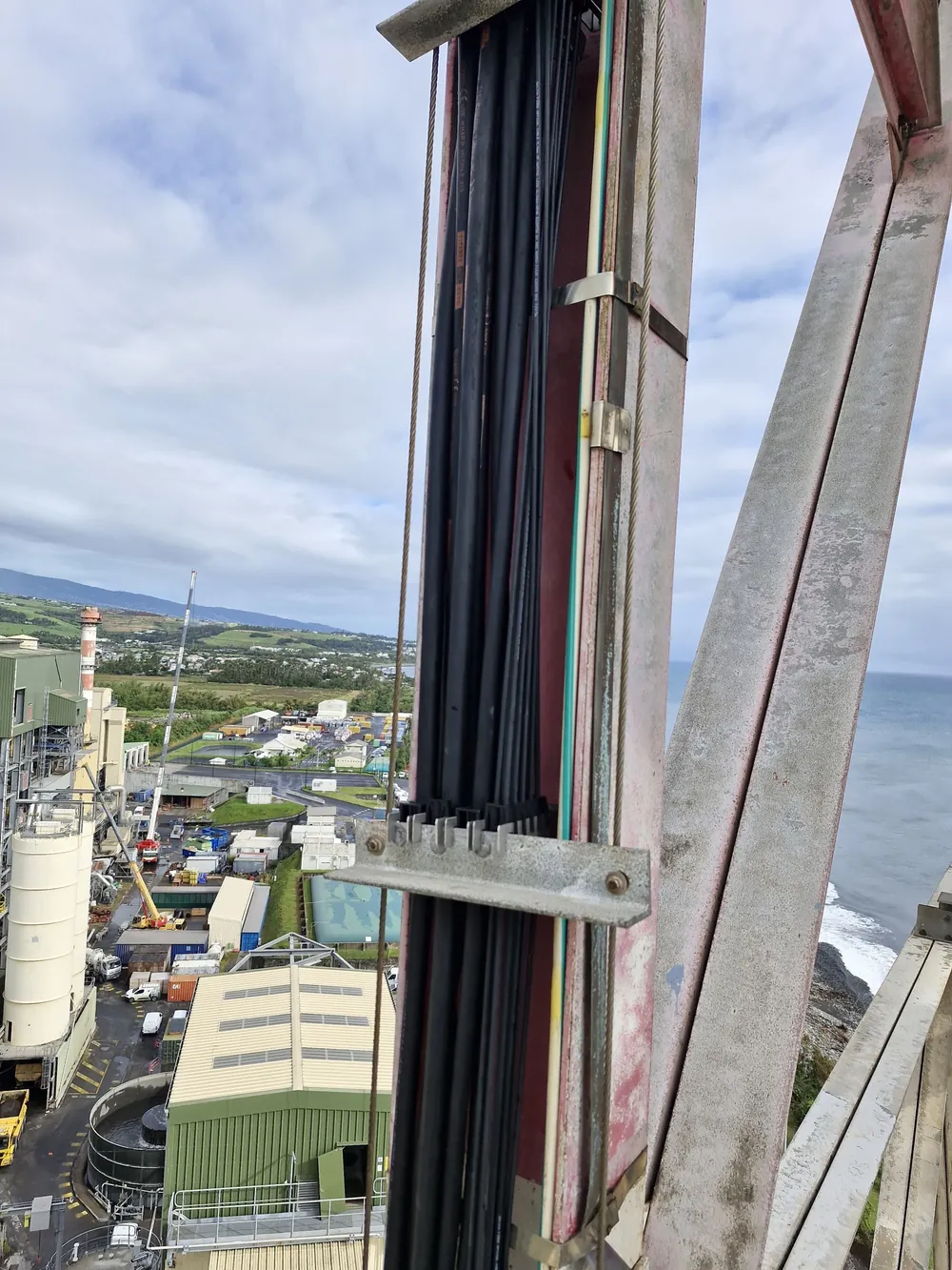 Faisceau de câbles fixé sur un pylône industriel, la côte et la mer en arrière-plan